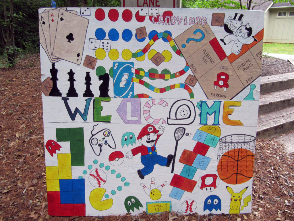 sign reading "welcome" surrounded by images associated with games such as cards, chess pieces, tetris piecs, Mario, a basketball, etc.